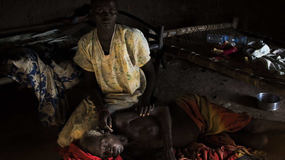 Abang Akok lies on the floor of her family home as one of her daughters brushes flies from her