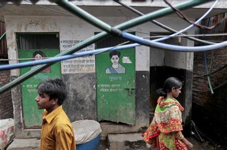 In this June 1, 2016 photo, Bangladeshis walk past a public toilet in a slum area in Dhaka, Bangladesh. Bangladesh's overpopulated urban areas are proving to be more of a challenge in the campaign for sanitation, mostly because the opportunity for contaminating water supply is much higher.