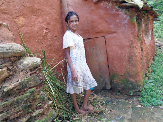Sangita stands beside the chhaugoth (shed for menstruating women) near her home. Its door is almost half her size, and she has to stay here every month when she menstruates. (Sabita)