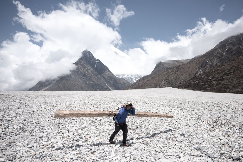 A volunteer carries a wooden beam across scree formed by one of the huge landslides near Kyanjin Gompa